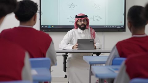 الاستفادة من التقنيات المتطورة في التعلم والدراسة، تطور طرائق التدريس في مدارس المملكة، المناهج المطورة والتعليم الالكتروني، طلاب عربيين خليجيين سعوديين يجلسون في مقاعدهم وأمامهم مدرس سعودي يستخدم التابلت فى الشرح