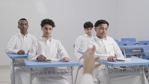 الإستعداد للعام الدراسي الجديد، التعليم في السعودية، تأدية الواجبات المدرسية، العودة إلى المدارس، مجموعة من الطلاب العربيين الخليجيين السعوديين يجلسون في مقاعدهم ويقومون بحل الواجب