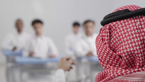 التربية والتعليم بالمناهج المقررة للتلاميذ، تصوير مقرب لمعلم عربي خليجي سعودي يرتدي الشماغ يقوم بمناقشة الدروس مع طلابه، المشاركة الفعالة للطلاب مع المدرسين، جودة التعليم في السعودية،مجموعه من الطلاب يقومون بكتابة الدروس