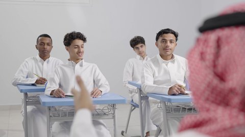 ايماءات الحماس لمعرفة الجواب الصحيح، المشاركة والتفاعل داخل الفصل الدراسي، طلاب عربيين خليجيين سعوديين يجلسون في مقاعدهم يرفعون ايديهم للاجاية ، التربية والتعليم بالمناهج المقررة للطلاب في المملكة العربية السعودية