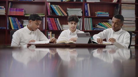 مدارس المملكة المبتكره، استخدام التقنية الحديثة، الاستمتاع بقراءة الكتب المدرسية، مجموعة من طلاب عربيون خليجيون سعودوين يجلسون في المكتبة المدرسية، تأدية الواجبات المدرسية