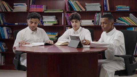 تأدية الواجبات المدرسية، استخدام التقنية الحديثة، الاستمتاع بقراءة الكتب المدرسية، مجموعة من طلاب عربيون خليجيون سعودوين يجلسون في المكتبة المدرسية، التعليم في المملكة العربية السعودية