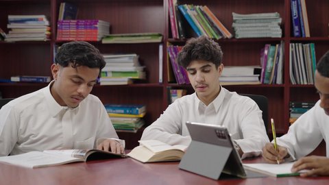 استخدام التقنية الحديثة، الاستمتاع بقراءة الكتب المدرسية، تصوير مقرب لمجموعة من طلاب عربيون خليجيون سعودوين يجلسون في المكتبة المدرسية، تأدية الواجبات المدرسية، التعليم في المملكة العربية السعودية