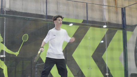 التدرب على إتقان لعبة البادل، رياضات شبابية وأنشطة ترفيهية، القيام بتمرينات رياضة التنس، خوض المباريات والبطولات بتحدي وعزيمة، شاب عربي خليجي سعودي يرتدي ملابس رياضية يلعب مباراة كرة المضرب، تعابير وإيماءات تدل على الحماس والاندماج بالتمرين