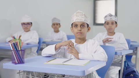 طلاب عربيين خليجيين عمانيين يجلسون في مقاعدهم يرفعون ايديهم للاجاية ، التربية والتعليم بالمناهج المقررة للطلاب في سلطنة عمان ، المشاركة والتفاعل داخل الفصل الدراسي،ايماءات الحماس لمعرفة الجواب الصحيح