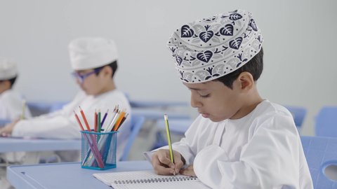 الإستعداد للعام الدراسي الجديد،تأدية الواجبات المدرسية، التعليم في سلطنة عمان، العودة إلى المدارس، مجموعة من الطلاب العربيين الخليجيين العمانيين يرتدون الدشداشة والكمة يجلسون في مقاعدهم ويقومون بحل الواجب