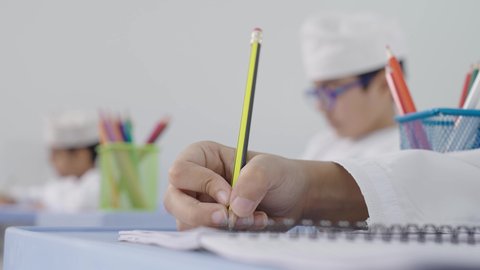 تأدية الواجبات المدرسية، الإستعداد للعام الدراسي الجديد، التعليم في سلطنة عمان، العودة إلى المدارس، مجموعة من الطلاب العربيين الخليجيين العمانيين يرتدون الدشداشة والكمة يجلسون في مقاعدهم ويقومون بحل الواجب