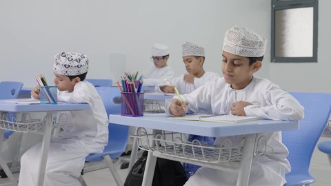 التعليم في سلطنة عمان،تأدية الواجبات المدرسية، الإستعداد للعام الدراسي الجديد، العودة إلى المدارس، مجموعة من الطلاب العربيين الخليجيين العمانيين يرتدون الدشداشة والكمة يجلسون في مقاعدهم ويقومون بحل الواجب