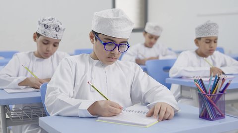 الإستعداد للعام الدراسي الجديد، تأدية الواجبات المدرسية، التعليم في سلطنة عمان، العودة إلى المدارس، مجموعة من الطلاب العربيين الخليجيين العمانيين يرتدون الدشداشة والكمة يجلسون في مقاعدهم ويقومون بحل الواجب