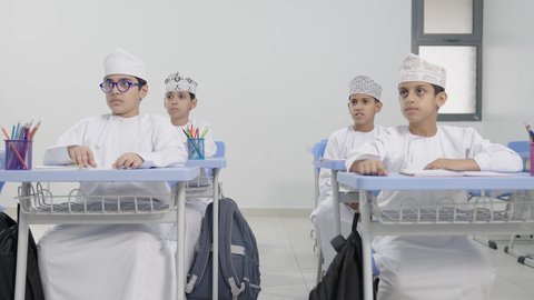 ايماءات الحماس لمعرفة الجواب الصحيح، المشاركة والتفاعل داخل الفصل الدراسي،طلاب عربيين خليجيين عمانيين يجلسون في مقاعدهم يرفعون ايديهم للاجاية ، التربية والتعليم بالمناهج المقررة للطلاب في سلطنة عمان