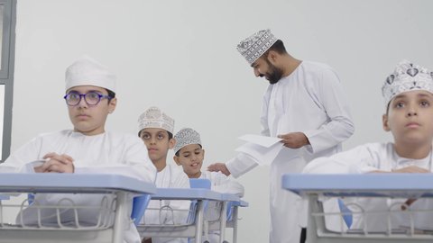 التربية والتعليم بالمناهج المقررة للتلاميذ،المشاركة الفعالة للطلاب مع المدرسين، معلم عربي خليجي عماني يرتدي الدشداشة والكمة يقوم بمناقشة الدروس مع طلابه، جودة التعليم في سلطنة عمان ، حوارات ودية بين الاستاذ والطلاب