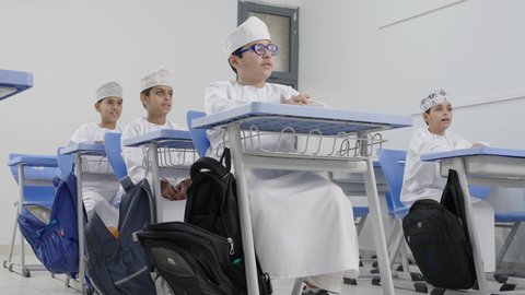 العودة إلى المدارس، تأدية الواجبات المدرسية، الإستعداد للعام الدراسي الجديد، التعليم في سلطنة عمان،  مجموعة من الطلاب العربيين الخليجيين العمانيين يرتدون الدشداشة والكمة يجلسون في مقاعدهم ويقومون بحل الواجب