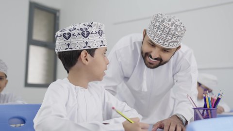 جودة التعليم في سلطنة عمان ، المشاركة الفعالة للطلاب مع المدرسين، معلم عربي خليجي عماني يرتدي الدشداشة والكمة يقوم بمناقشة الدروس مع طلابه، التربية والتعليم بالمناهج المقررة للتلاميذ، حوارات ودية بين الاستاذ والطلاب