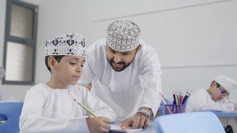 المشاركة الفعالة للطلاب مع المدرسين، معلم عربي خليجي عماني يرتدي الدشداشة والكمة يقوم بمناقشة الدروس مع طلابه، جودة التعليم في سلطنة عمان ، التربية والتعليم بالمناهج المقررة للتلاميذ، حوارات ودية بين الاستاذ والطلاب