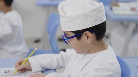Performing school assignments, preparing for the new school year, education in the Sultanate of Oman, back to school, a group of Arab Gulf Omani students wearing the dishdasha and kumma sitting in their seats and doing their homework.