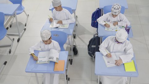 التعليم في سلطنة عمان،تأدية الواجبات المدرسية، الإستعداد للعام الدراسي الجديد، العودة إلى المدارس، مجموعة من الطلاب العربيين الخليجيين العمانيين يرتدون الدشداشة والكمة يجلسون في مقاعدهم ويقومون بحل الواجب