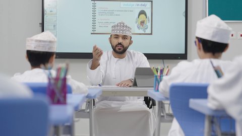 جودة التعليم الالكتروني، الاستفادة من التقنيات والتكنولوجيا الحديثة في التعلم والدراسة، طلاب عربيين خليجيين عمانيين يجلسون في مقاعدهم وأمامهم معلم يستخدم جهاز التابلت، تطور طرائق التدريس في مدارس سلطنة عمان