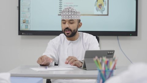 Developed curricula and e-learning, benefiting from modern technologies and techniques in learning and studying, two Arab Gulf students from Oman sitting in their seats with a teacher using a tablet in front of them, the evolution of teaching methods in schools in the Sultanate of Oman.