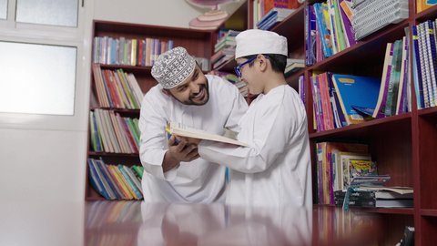 معلم عربي خليجي عماني يرتدي الدشداشة والكمة يقوم بمناقشة الكتاب مع طلابه، المشاركة الفعالة للطلاب مع المدرسين، الاستمتاع بقراءة الكتب المدرسية ، جودة التعليم في سلطنة عمان ، مفهوم التعليم والثقافة ، حوارات ودية بين الاستاذ والطلاب