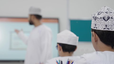 الاستفادة من التقنيات والتكنولوجيا الحديثة في التعلم والدراسة، المناهج المطورة والتعليم الالكتروني، تطور طرائق التدريس في مدارس سلطنة عمان، طلاب عربيين خليجيين سعوديين يجلسون في مقاعدهم وأمامهم مدرس عماني يستخدم جهاز التابلت