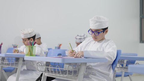 العودة إلى المدارس، تأدية الواجبات المدرسية، الإستعداد للعام الدراسي الجديد، التعليم في سلطنة عمان ،مجموعة من الطلاب العربيين الخليجيين العمانيين يرتدون الدشداشة والكمه يجلسون في مقاعدهم ويقومون بحل الواجب