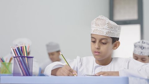 تأدية الواجبات المدرسية، الإستعداد للعام الدراسي الجديد، التعليم في سلطنة عمان ، العودة إلى المدارس، مجموعة من الطلاب العربيين الخليجيين العمانيين يرتدون الدشداشة والكمه يجلسون في مقاعدهم ويقومون بحل الواجب