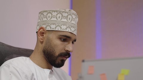 Close-up shot of an Emirati Gulf Arab man wearing a kandura and ghutrah looking at something, with gestures of engagement and focus.