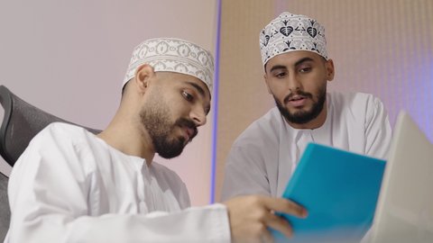 التعاون والتفاهم بين الزملاء ووضع الخطط الاستراتيجية، عقد اجتماع داخل مقر الشركة، تصوير مقرب لموظفان عربيان خليجيان اماراتيان يرتديان الدشداشة و الكمة يتعلمان اساليب العمل والتطوير المهني، النقاش والتفاهم بين الموظفين، تبادل الخبرات والمعلومات لتحقيق الاهداف، روح الفريق الواحد والعمل الجماعي