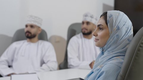 Training employees on work policies and tasks to achieve goals, gestures of happiness and joy, exchanging successful experiences and information, a close-up side shot of an Omani Gulf Arab woman wearing an abaya and hijab sitting in a meeting room inside the company headquarters with her colleagues.