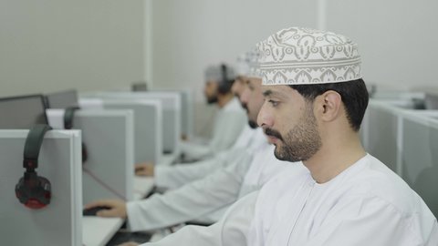 الانجاز و التفوق في المرحلة الجامعية، التربية و التعليم بالمناهج المقررة، مجموعه من الطلاب العربيون الخليجيون العمانيون يرتدون الدشداشة و الكمة يقومون بالنظر الى الحاسب المحمول بايماءات الاندماج و التركيز