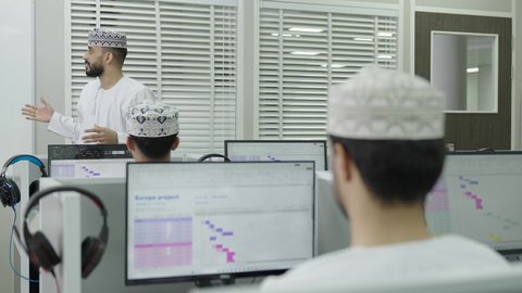 استخدام التقنية الحديثة، مفهوم التعليم في سلطنه عمان، معلم عربي خليجي عماني يرتدي الدشداشة و الكمة يقوم بشرح الدرس للطلاب، تصوير من الخلف لمجموعه من الطلاب يجلسون امام الحاسب المحمول يستمعون الى المحاضرة بايماءات الاندماج و التركيز