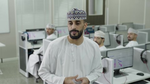 التعليم في سلطنه عمان، التفاعل والمشاركة داخل الفصل الدراسي، تصوير مقرب لمعلم عربي خليجي عماني يرتدي الدشداشة و الكمة يقوم بشرح الدرس للطلاب، مجموعه من الطلاب يستمعون الى المحاضرة بايماءات الاندماج و التركيز