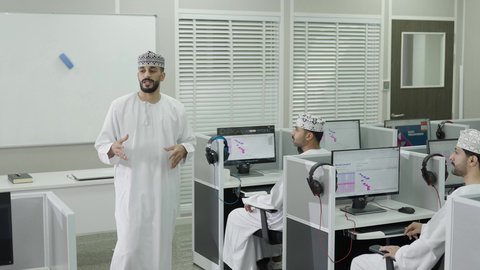 A Gulf Arab Omani teacher wearing a dishdasha and kumma is explaining the lesson to the students, with interaction and participation inside the classroom, education in the Sultanate of Oman, a group of students listening to the lesson with gestures of engagement and focus.