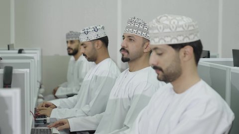 النشاط داخل الفصل الدراسي، استخدام جهاز تقني حديث في التعلم، المشاركة الفعالة للطلاب، طالب يرفع يدية للإجابة عن السؤال، مجموعه من الطلاب العرب الخليجيون العمانيون يرتدون الدشداشة و الكمه يقومون بالتفاعل اثناء المحاضرة الجامعية