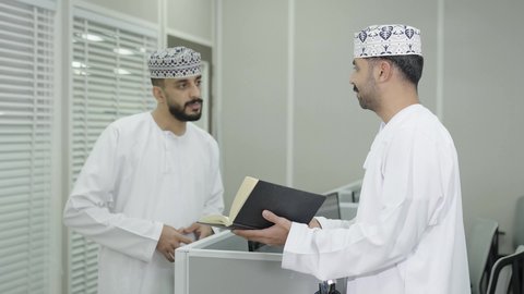 معلم عربي خليجي إماراتي يرتدي الكندورة والغترة يقوم بشرح شي ما، مفهوم الاجتهاد وطلب التفوق، طالب عربي خليجي عماني يرتدي الدشداشة و الكمة يمسك بيديه كتاب دراسي