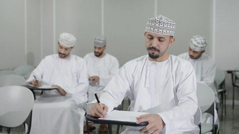 تعابير تدل على التفكير العميق والتركيز، التعليم في سلطنه عمان، الاجتهاد في الدراسة لتحقيق النجاح والتميز الأكاديمي, اهداف التربية و التعليم، مجموعه من الطلاب العرب الخليجيون العمانيون يرتدون الدشداشة و الكمة يقومون بحل اسئله الامتحان