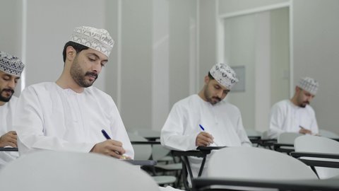 ايماءات التفكير و التركيز في اسئلة الاختبار، نهاية الفصل الدراسي, تصوير مقرب لمجموعة من الطلاب العربي الخليجيون العمانيون يرتدون الدشداشة و الكمة يقومان بحل الامتحان, التعليم في سلطنه عمان, المشاركة الفعالة للطلاب, اهداف التربية و التعليم