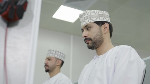 تصوير مقرب لطالبان عربيان خليجيان عمانيان يرتديان الدشداشة و الكمة يقومان بالنظر الى شيء ما ، ايماءات الاندماج و التركيز