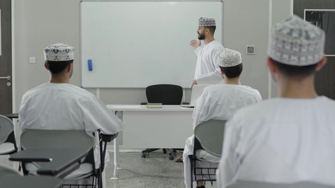 تركيز وانسجام الطلاب أثناء الاستماع إلى المحاضرة، تطوير أساليب التعليم الجامعي في سلطنه عمان، معلم عربي خليجي عماني يرتدي الدشداشة و الكمة يقوم بشرح المحاضرة للطلاب، ورش عمل ودورات تدريبية، التعليم الجامعي العماني