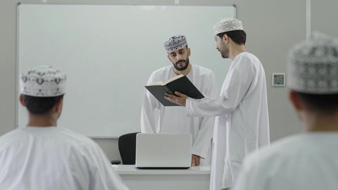 ورش عمل ودورات تدريبية، تطوير أساليب التعليم الجامعي في سلطنه عمان، الإنتباه والتركيز والإستماع إلى المحاضرة، طالب عربي خليجي عماني يرتدي الدشداشة و الكمة يمسك بيديه كتاب و يقوم بالمناقشة مع المعلم، التعليم الجامعي العماني