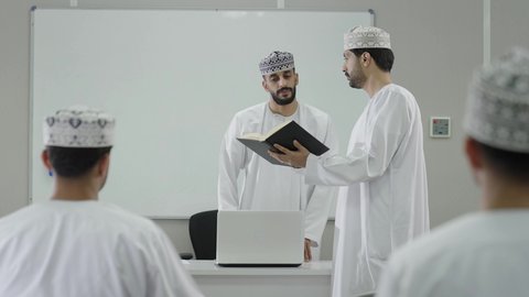 تطوير أساليب التعليم الجامعي في سلطنه عمان، الإنتباه والتركيز والإستماع إلى المحاضرة، طالب عربي خليجي عماني يرتدي الدشداشة و الكمة يمسك بيديه كتاب و يقوم بالمناقشة مع المعلم، ورش عمل ودورات تدريبية، التعليم الجامعي العماني