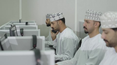 استخدام التقنية الحديثة، تبادل الأحاديث والدردشات حول المواضيع الدراسيه، الجامعات والكليات العمانية ،تصوير مقرب  لطالبان عربيان خليجيان عمانيان يرتديان الدشداشة و الكمة يجلسان  في المحاضرة،  الاشارة الى شاشة الحاسوب، شاب عربي خليجي عماني يقوم باجراء مكالمه هاتفية عبر الهاتف المحمول