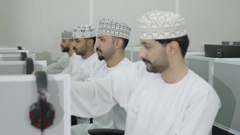 ايماءات الاندماج و التركيز، الدراسة و الاجتهاد من اجل التفوق، التعليم في سلطنه عمان,  تصوير مقرب لطلاب عربيون خليجيون عمانيون يرتدون الدشداشة و الكمة يجلسون فى المحاضرة يقومون بوضع سماعات الراس على  اذنهم لاستماع الشرح