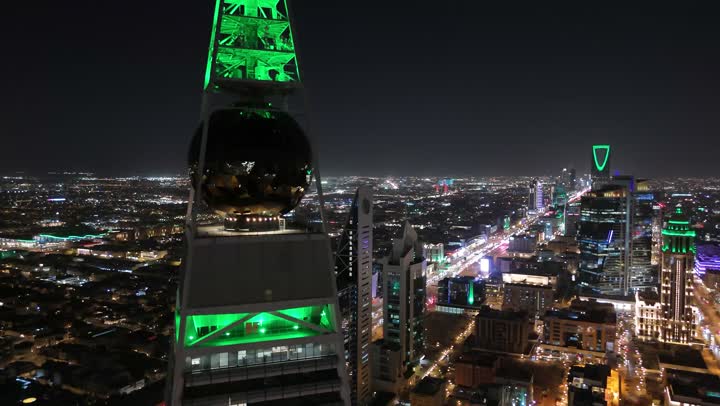 The sophisticated architectural style of the Olaya Towers, King Fahd Road in the Kingdom, the celebration of Saudi National Day on September 23, lighting skyscrapers, tourist facilities and hotels in green, the Saudi economic and urban renaissance, an aerial drone shot of the Al Faisaliah Tower in Riyadh
