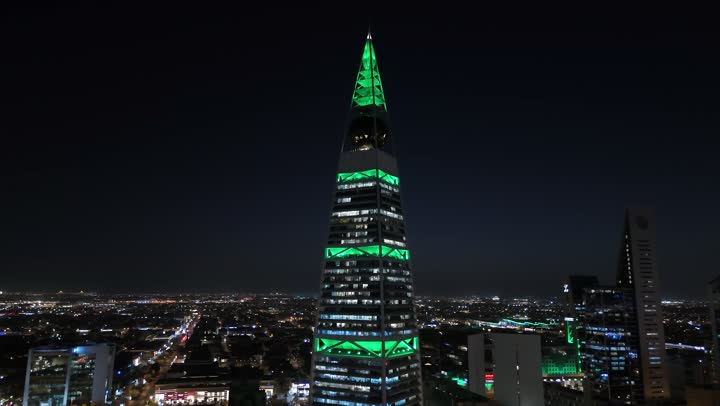 Saudi National Day on September 23: Skyscrapers, tourist facilities, and hotels lit up in green. Saudi Arabia's economic and urban renaissance. Aerial drone footage of the Al Faisaliah Tower in Riyadh. The sophisticated architectural style of the Olaya Towers. King Fahd Road in the Kingdom.