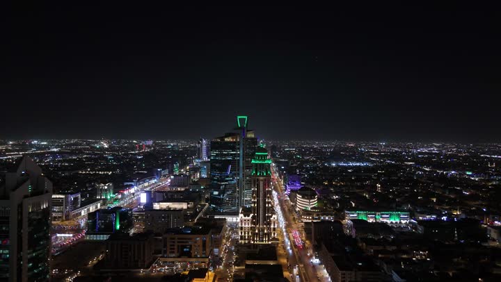 Focus on the infrastructure of Riyadh, the architectural art of towers and skyscrapers in the Kingdom of Saudi Arabia, paved streets and roads, commercial and residential facilities and modern buildings, aerial drone photography of traffic in the capital's illuminated streets at night
