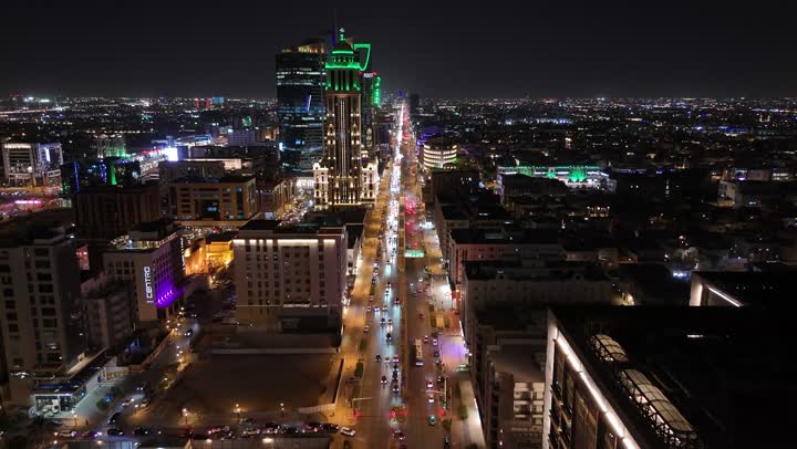 Paved streets and roads, commercial and residential facilities and modern buildings, aerial drone footage of traffic in the capital's illuminated streets at night, attention to infrastructure in Riyadh, and the architectural art of towers and skyscrapers in the Kingdom of Saudi Arabia.