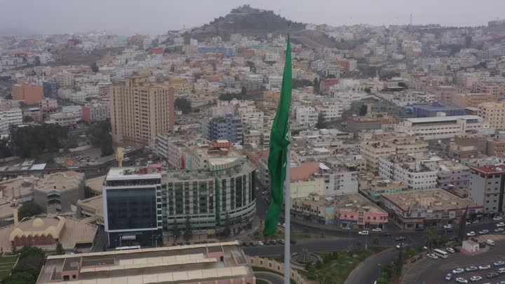 سارية العلم السعودي الأخضر المرفرف في الهواء في دوار الملك فيصل، الفخر والاعتزاز بالانتماء الى الوطن, المعالم المشهورة في مدينة أبها بمنطقة عسير جنوب غرب المملكة