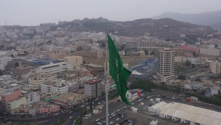 سارية العلم السعودي الأخضر المرفرف في الهواء في دوار الملك فيصل، الفخر والاعتزاز بالانتماء الى الوطن, المعالم المشهورة في مدينة أبها بمنطقة عسير جنوب غرب المملكة