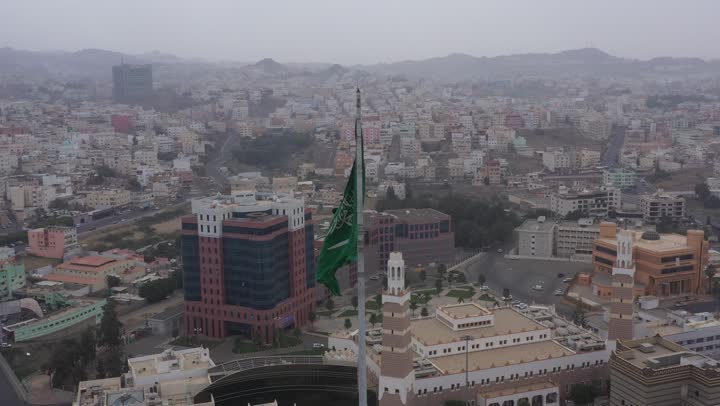 سارية العلم السعودي الأخضر المرفرف في الهواء في دوار الملك فيصل، الفخر والاعتزاز بالانتماء الى الوطن, المعالم المشهورة في مدينة أبها بمنطقة عسير جنوب غرب المملكة